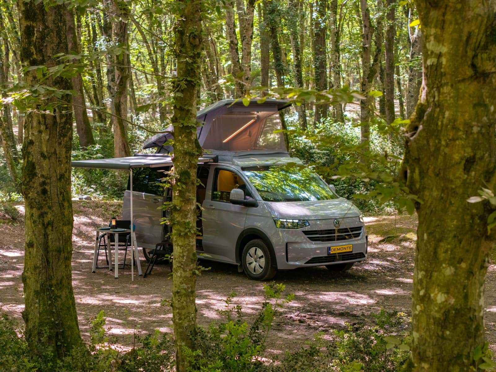 New Cappadocia on the new-generation VW Transporter in the forest, pop-up roof and awning open with a camp table underneath