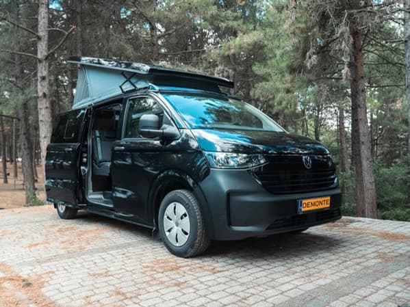 The black Olympos in a pine forest with the pop-up roof raised and the side door slid open