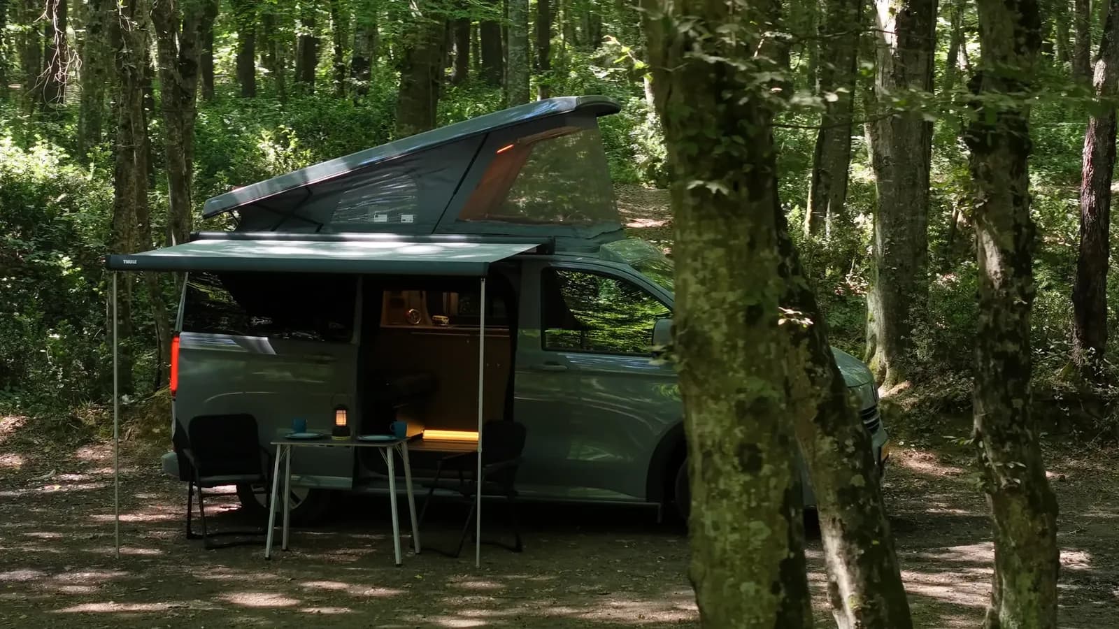 Orman kampında pop-up tavanı ve tentesi açık Demonte Karavan campervan, ağaçların arasından kuşbakışı