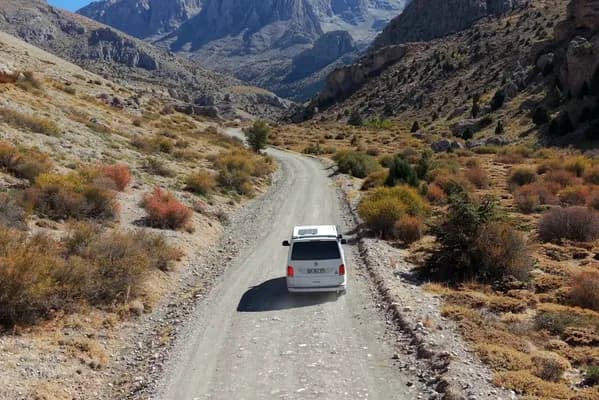 Aladağlar’da çakıl bir dağ yolunda ilerleyen Demonte Karavan campervan, ilerisinde sarp kireçtaşı zirveleri