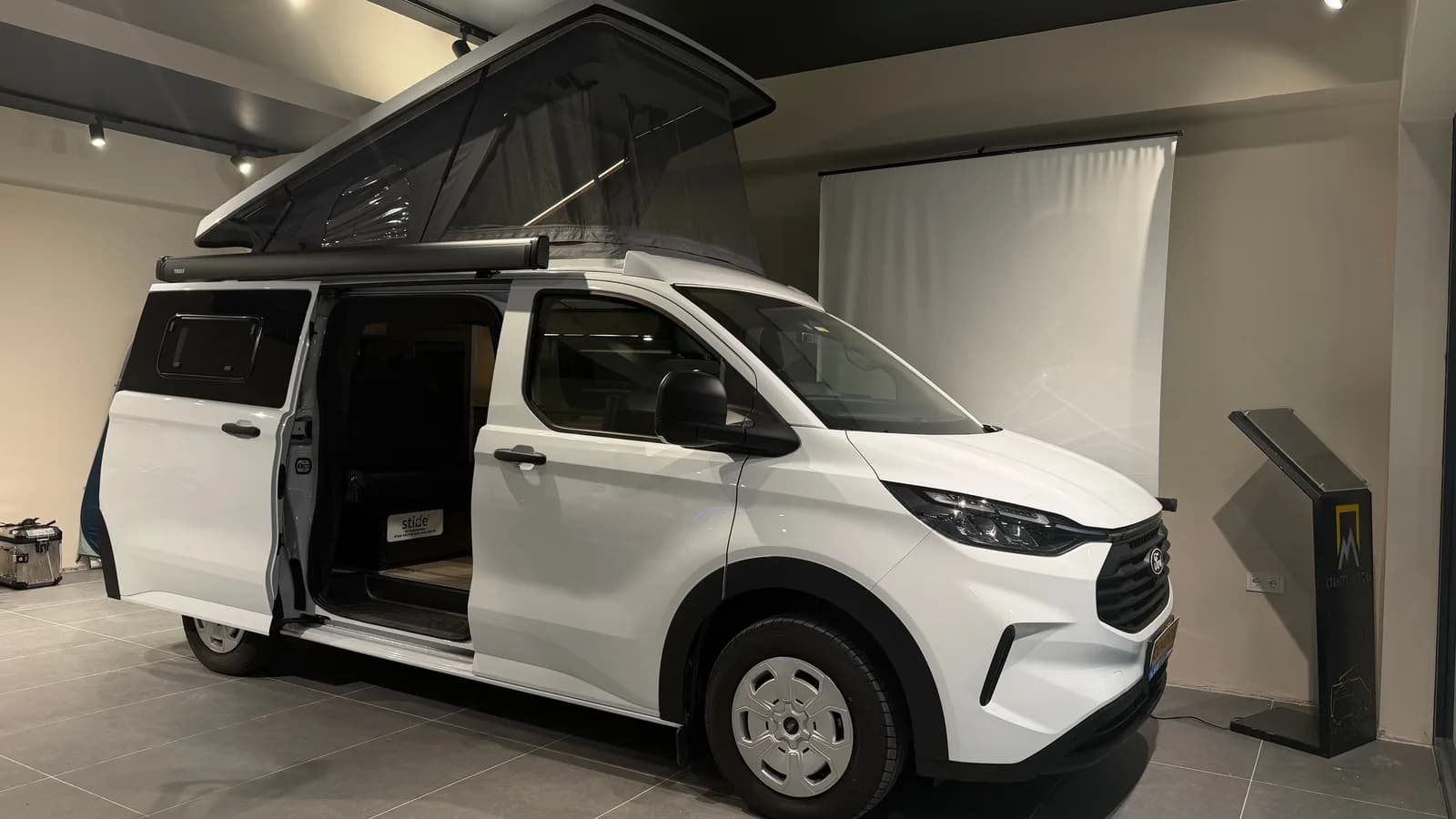 White Ford Transit Custom Assos in the showroom with the SCA pop-up roof raised and side door open