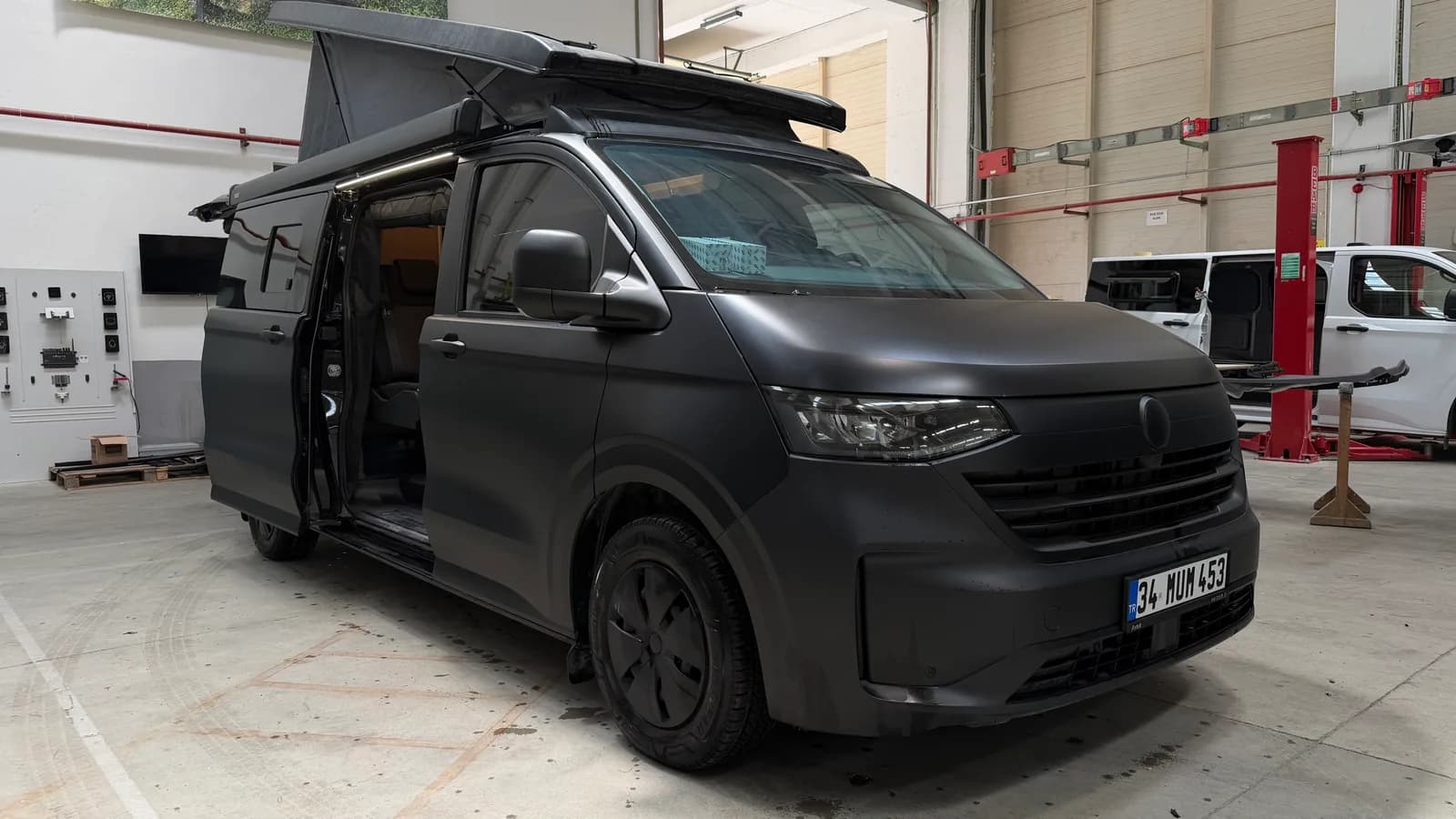 Matte black Volkswagen Transporter 4x4 Olympos in the workshop with the SCA pop-up roof and side door open