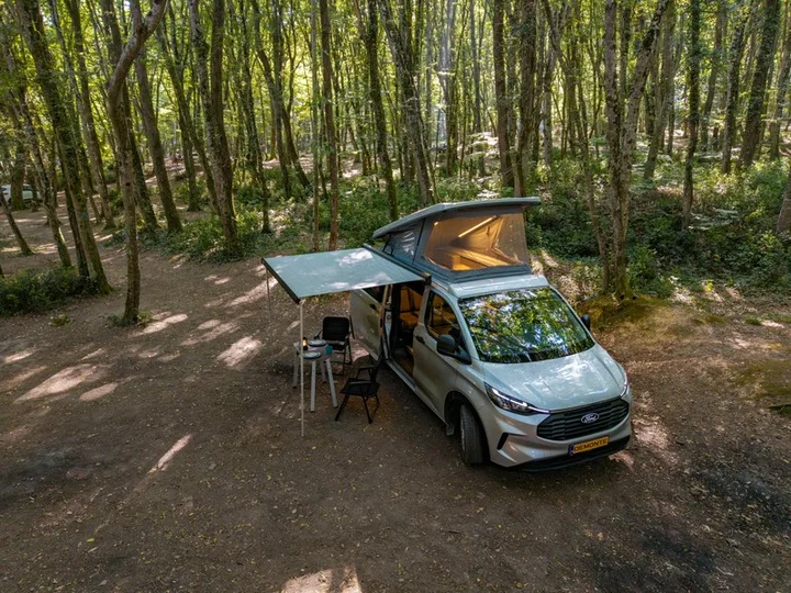 Assos zwischen den Bäumen, Seitentür offen und Camp unter der Markise aufgebaut