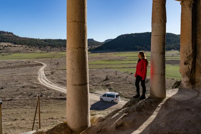 Eine Reisende blickt zwischen antiken Säulen hinab ins Tal auf den dort geparkten Cappadocia