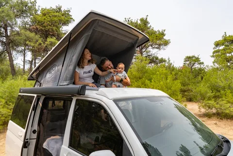 Eine Mutter mit ihren Kindern im aufgestellten Dachbett über dem Campingplatz