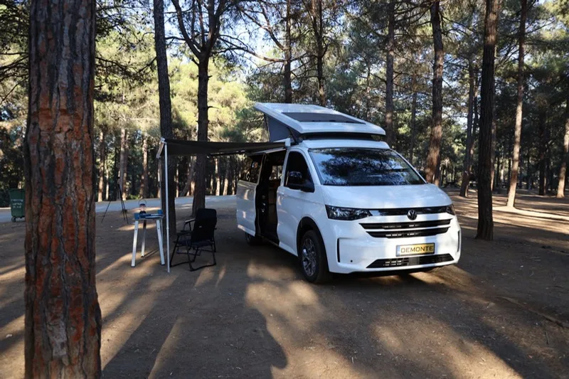 Efes set up in a pine forest with the roof raised, side door open and a table and chairs in front