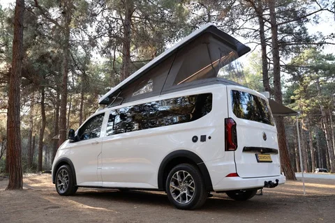 The long-wheelbase side profile of the Efes with the pop-up roof raised and pine forest behind