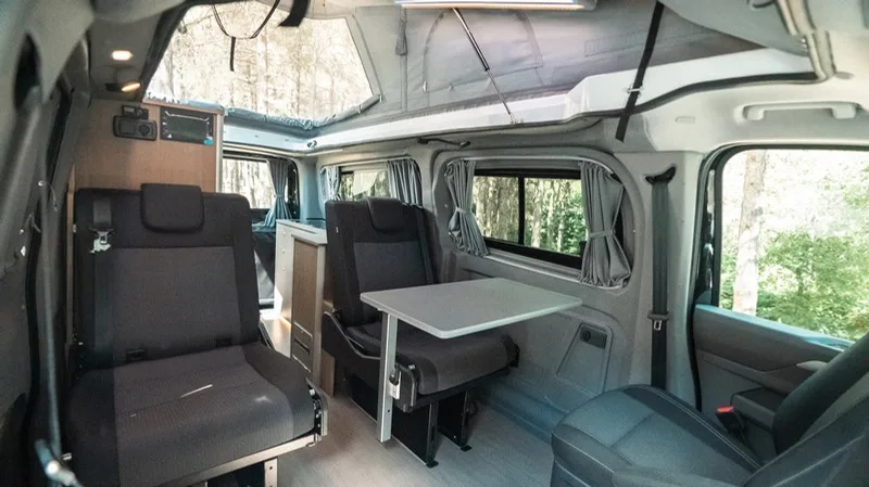 The living area of the Olympos with facing seats, a folding table between them and light coming through the raised roof