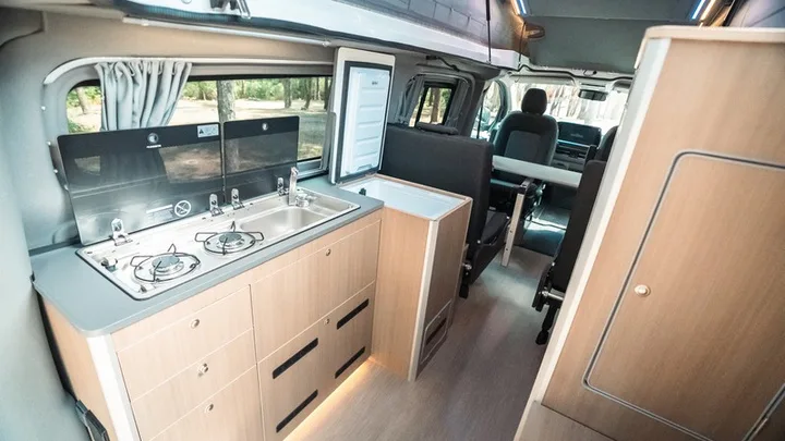 The Olympos galley with a glass-lid two-burner hob and sink, the fridge beside it and LED-lit drawers below