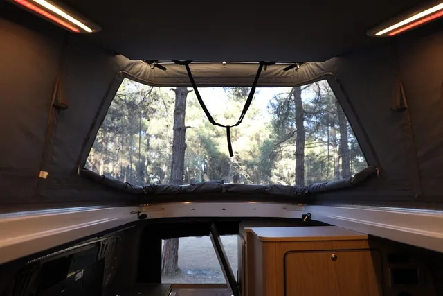Looking out at the pine forest from the roof bed of the Olympos, mesh windows open and an LED strip on each side