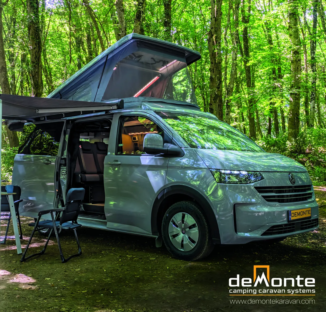 Demonte Karavan 2026 catalogue, page 1: cover — a VW Transporter in the forest with its pop-up roof and awning open, a camping chair beside it