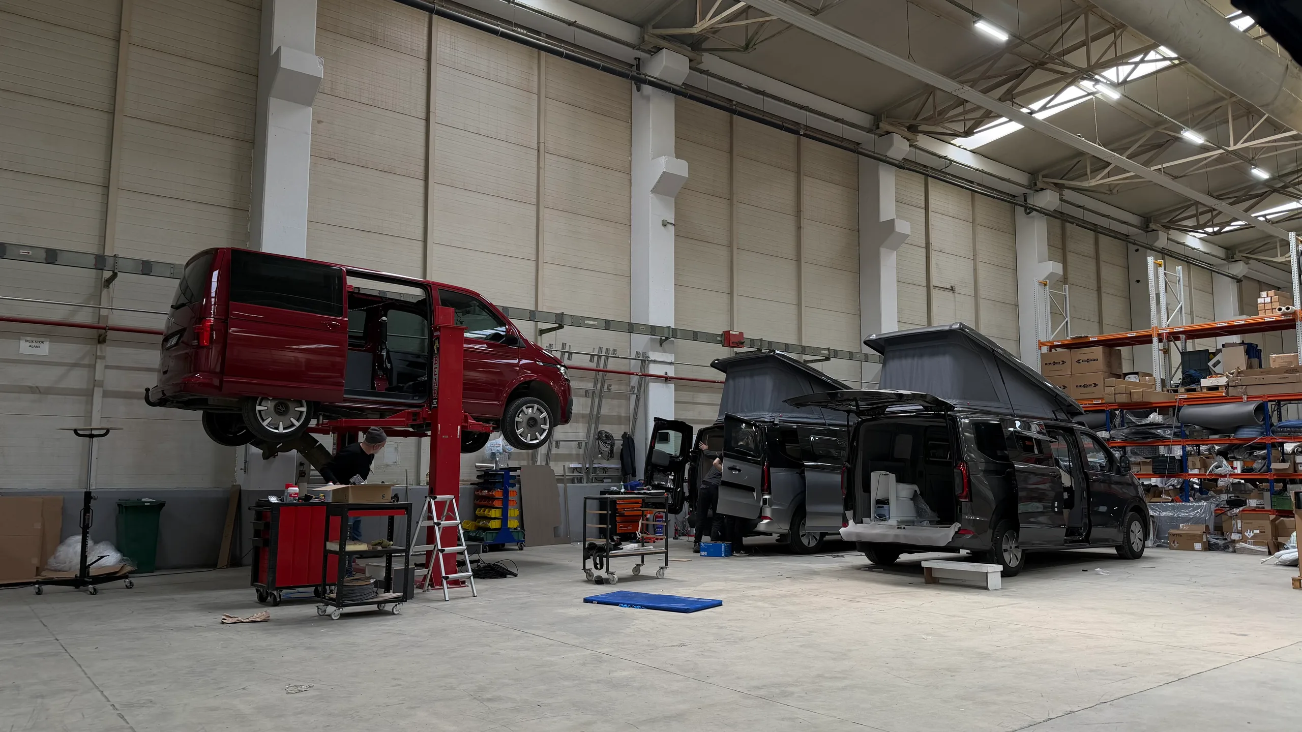A VW Transporter on the lift and two Ford Transit Customs under conversion with their pop-up roofs raised, at the Dilovası production facility