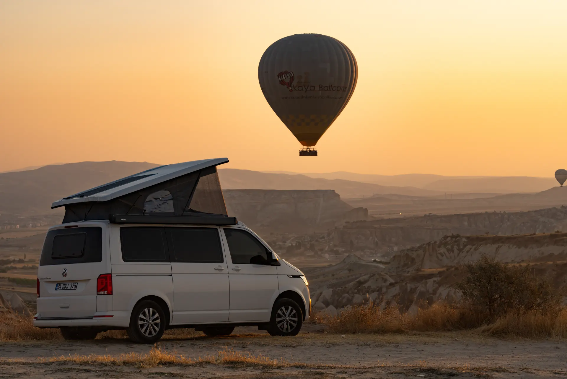 Ein einzelner Heißluftballon über dem kappadokischen Tal, darunter ein Demonte-Camper