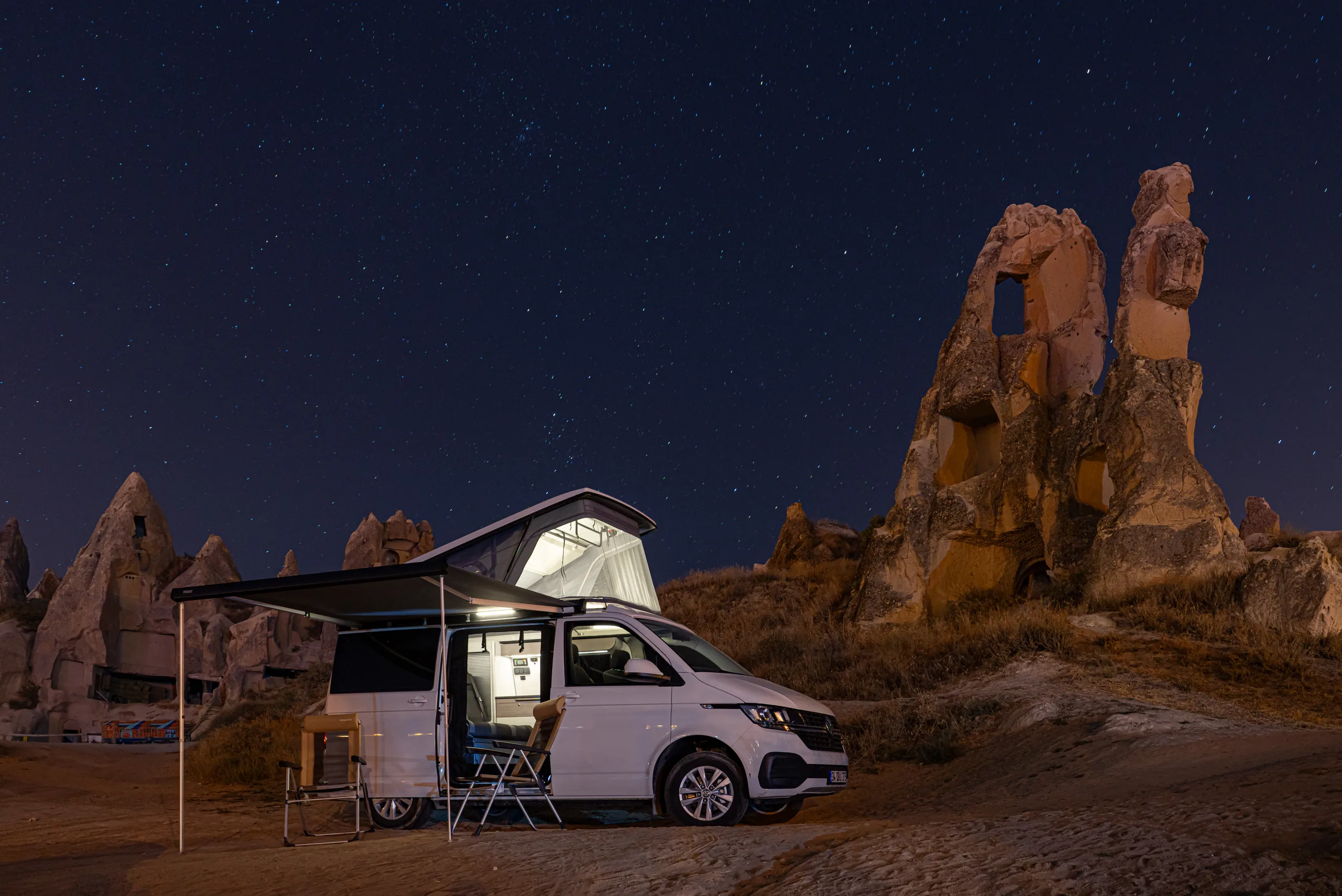 Demonte-Camper zwischen den Feenkaminen Kappadokiens unter Sternenhimmel, Markise ausgefahren und Innenraum beleuchtet