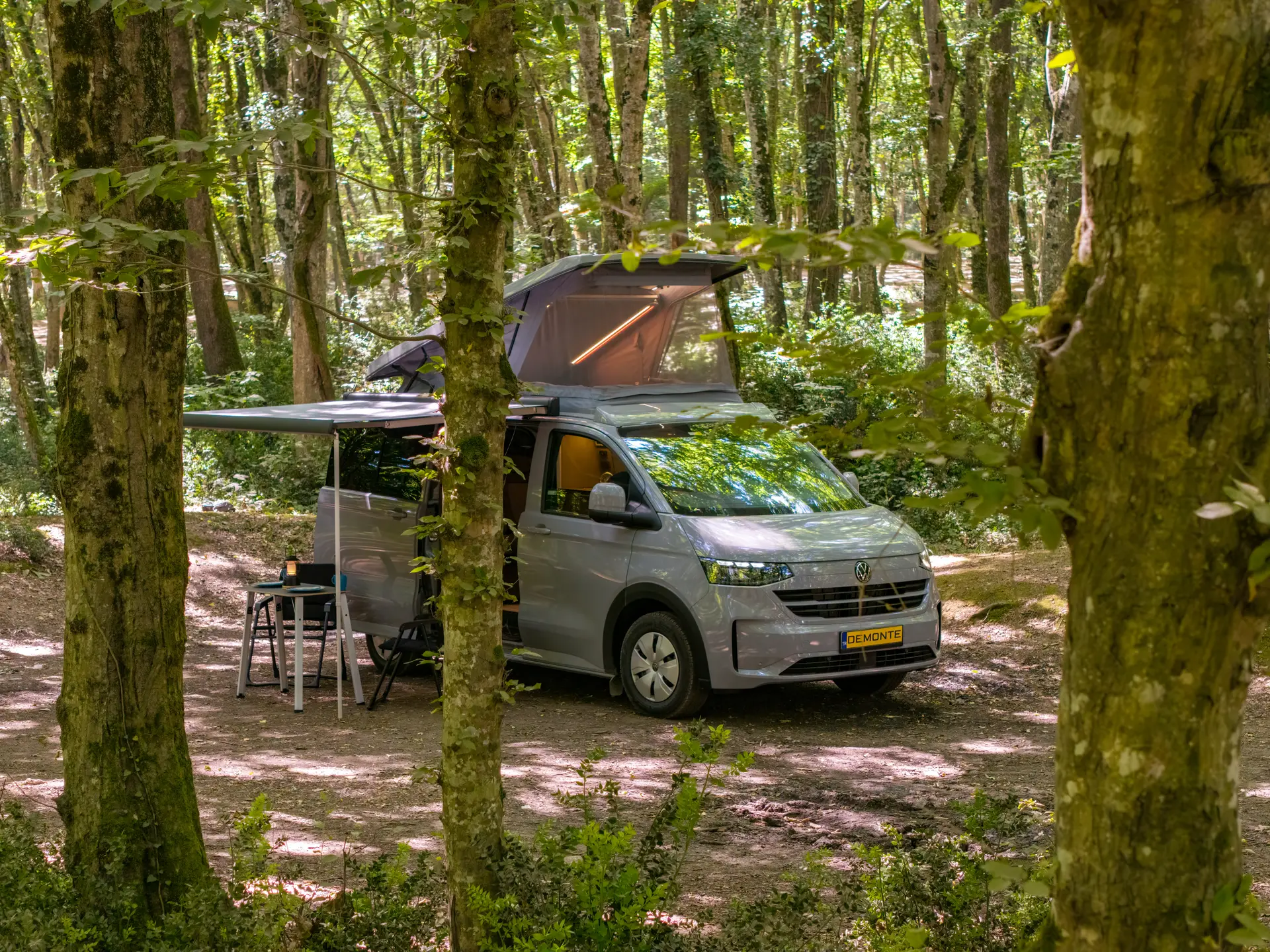 Demonte-Camper zwischen den Bäumen, Dach aufgestellt und Camp unter der Markise
